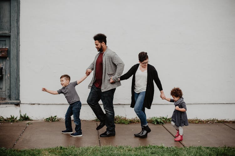 Man and woman holding hands with their kids and walking.